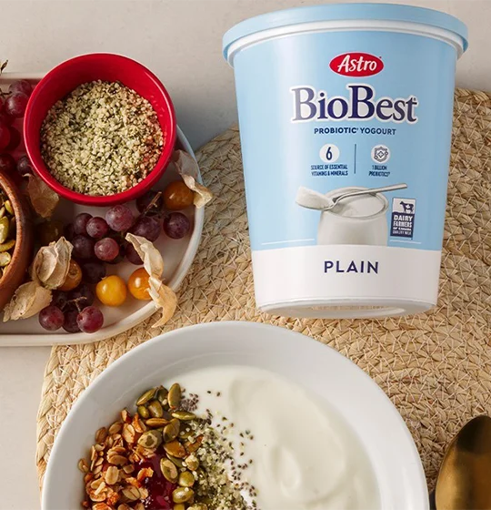 Astro BioBest yogurt tub on a table with various grains. A bowl of yogurt with grains added. Assorted fruit